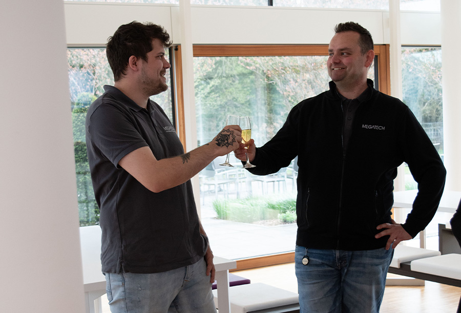 Zwei Männer stoßen mit einem Glas Sekt in der Hand an und lachen dabei