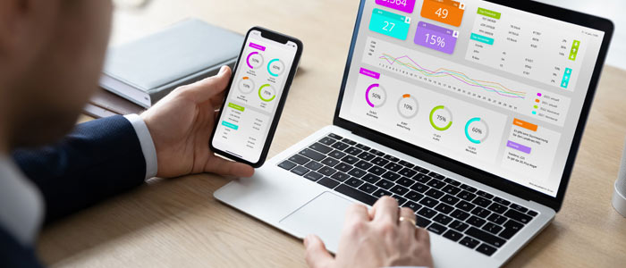 Mann sitzt an Schreibtisch und nutzt die Dashboard-Software zugleich am Laptop und am Smartphone.