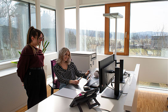 Kauffrau für Büromanagement Selina erklärt Anna am Schreibtisch wichtige Abläufe